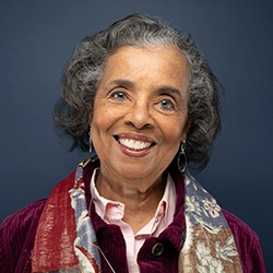 Ruth White smmiles into the camera against a dark blue background